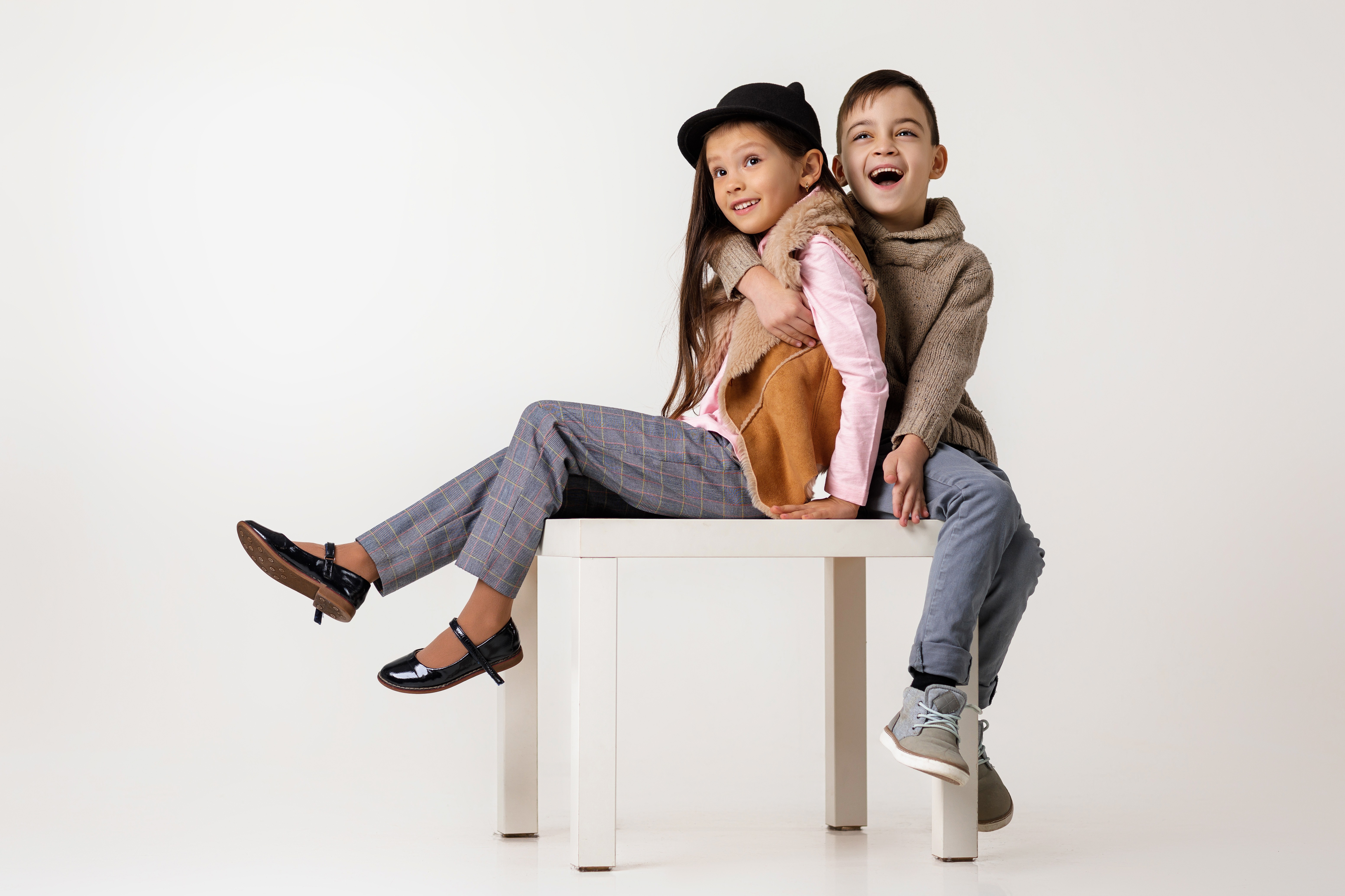 Two kids in fashionable outfits sitting on white table